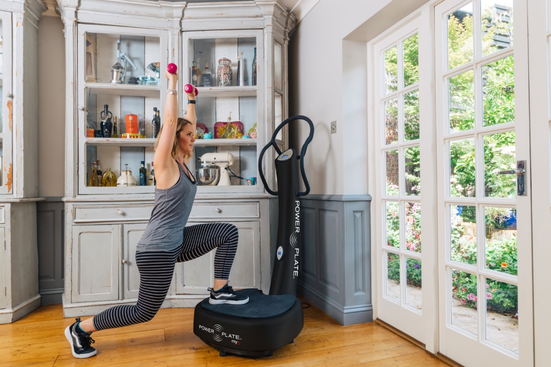 Woman performing a lunge with dumbbells on a Power Plate my5 vibration platform at home
