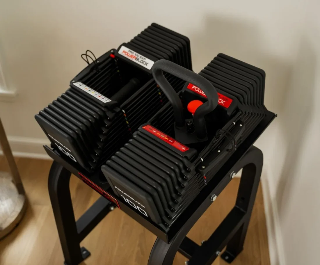 Close-up of PowerBlock dumbbells and a handle resting on the PowerBlock Home Rack Stand upper tray