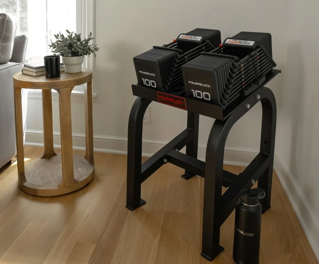 PowerBlock Home Rack Stand holding a pair of 100 lb adjustable dumbbells in a home gym